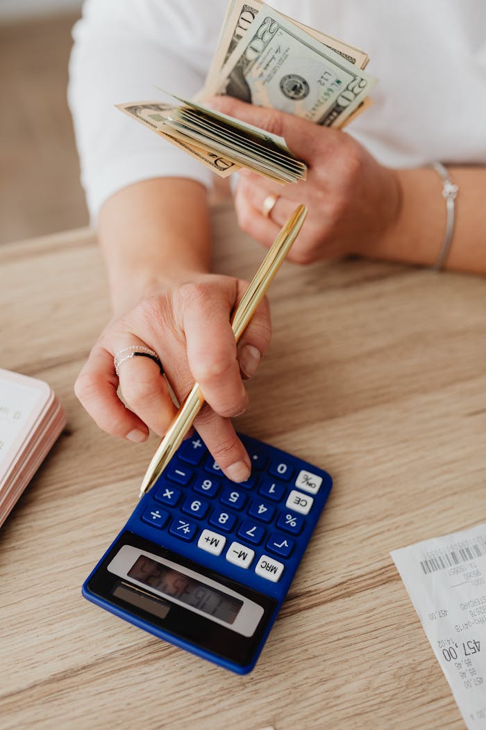 Close-up of hands counting cash and using a calculator for budgeting.